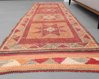 Könnte beinhalten: Ein roter, orangefarbener und beiger Teppich mit geometrischem Muster. Der Teppich hat einen Fransenrand.