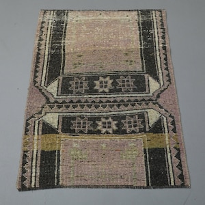 May include: A vintage rug with a pink and black geometric pattern. The rug has a faded look and is made of wool.