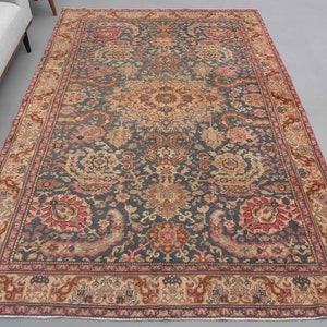 Könnte beinhalten: Ein antiker persischer Teppich mit einem dunkelblauen Hintergrund und komplizierten floralen Mustern in Rosa-, Beige- und Cremetönen. Der Teppich hat einen Rand mit einem sich wiederholenden Muster aus stilisierten Tieren und floralen Motiven.