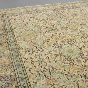 May include: A vintage rug with a cream background and intricate floral patterns in shades of brown, green, and pink. The rug has a border with a repeating design.