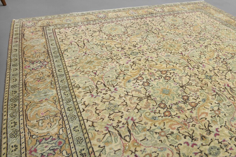 May include: A vintage rug with a cream background and intricate floral patterns in shades of brown, green, and pink. The rug has a border with a repeating design.