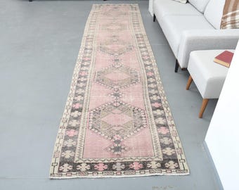 May include: A long, pink and cream runner rug with a geometric pattern. The rug has a faded, vintage look and is perfect for adding a touch of bohemian style to any room.