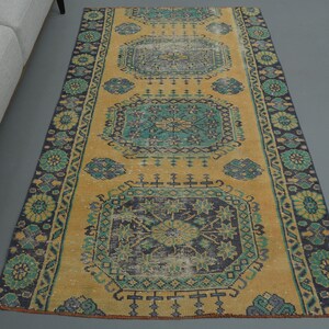Puede incluir: Una alfombra turca vintage de corredor con fondo amarillo y un patrón repetido de motivos florales azules y verdes. La alfombra tiene un borde con flecos.