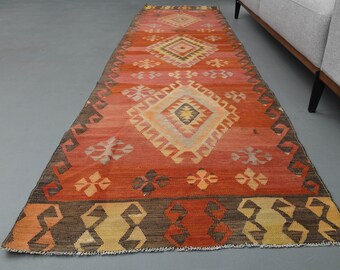 Könnte beinhalten: Ein langer, rechteckiger Teppich mit traditionellem türkischem Design. Der Teppich ist hauptsächlich rot mit braunen, gelben und cremefarbenen Akzenten. Das Design zeigt ein sich wiederholendes Rautenmuster mit komplizierten Details.