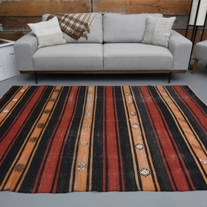 Può includere: Un tappeto a strisce con uno schema di colori nero, rosso e arancione. Il tappeto ha un design tradizionale con motivi geometrici.
