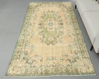 May include: A vintage rug with a beige background and a green floral pattern. The rug has a border with a geometric design.