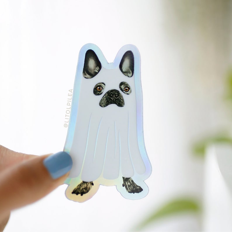 Pu&ograve; includere: Un adesivo olografico di un bulldog francese vestito da fantasma per Halloween. L'adesivo ha un costume da fantasma bianco con viso e orecchie nere. Il testo '@LITOLPILE'A &egrave; sull'adesivo.