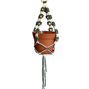 Peut inclure: Un porte-plante en macram&eacute; blanc et vert avec des perles en bois et un pot en terre cuite. Le porte-plante a une boucle en haut pour l'accrocher.