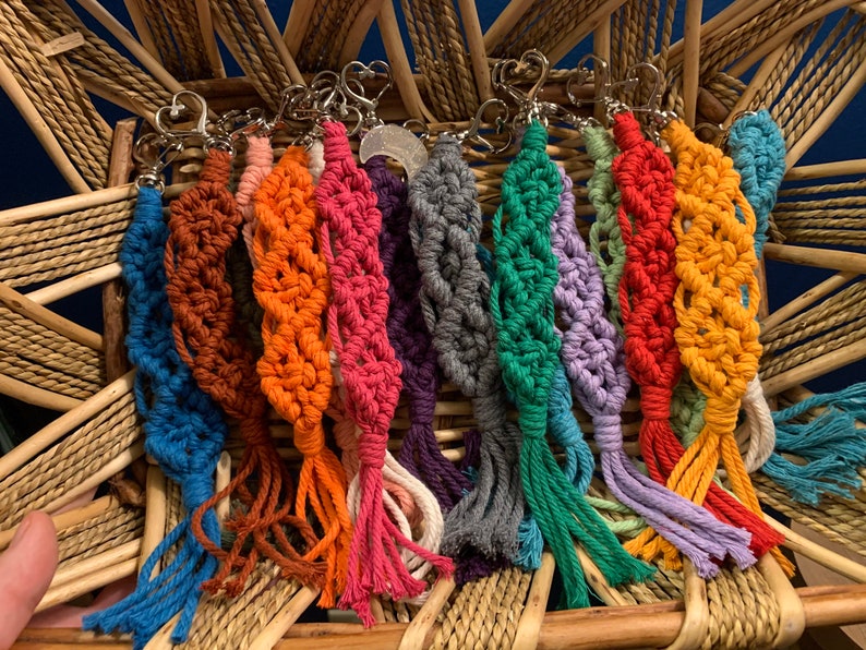 Puede incluir: Una colecci&oacute;n de llaveros de macram&eacute; coloridos con borlas. Los llaveros est&aacute;n hechos con una variedad de colores, incluyendo azul, naranja, rojo, verde, morado y amarillo. Cada llavero tiene un cierre de metal plateado.