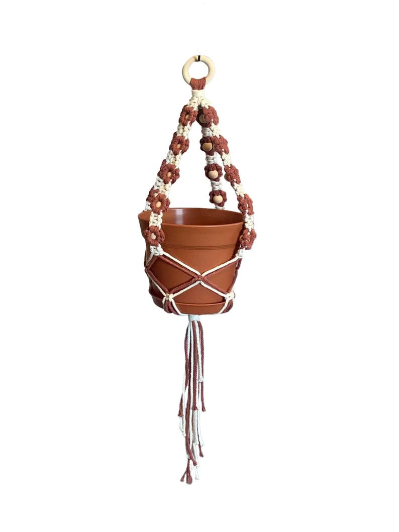 Peut inclure: Un porte-plante en macram&eacute; marron et blanc avec un anneau en bois en haut. Le porte-plante est muni d'un pot en terre cuite.