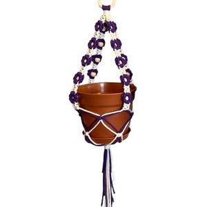 Peut inclure: Un porte-plante en macram&eacute; violet et blanc avec des perles en bois. Le porte-plante est muni d'un pot en terre cuite.