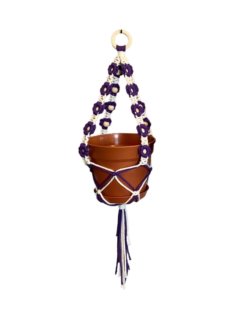Peut inclure: Un porte-plante en macram&eacute; violet et blanc avec des perles en bois. Le porte-plante est muni d'un pot en terre cuite.
