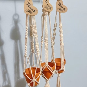 May include: Three macrame plant hangers with terracotta pots and heart-shaped tags that say "Thank you".