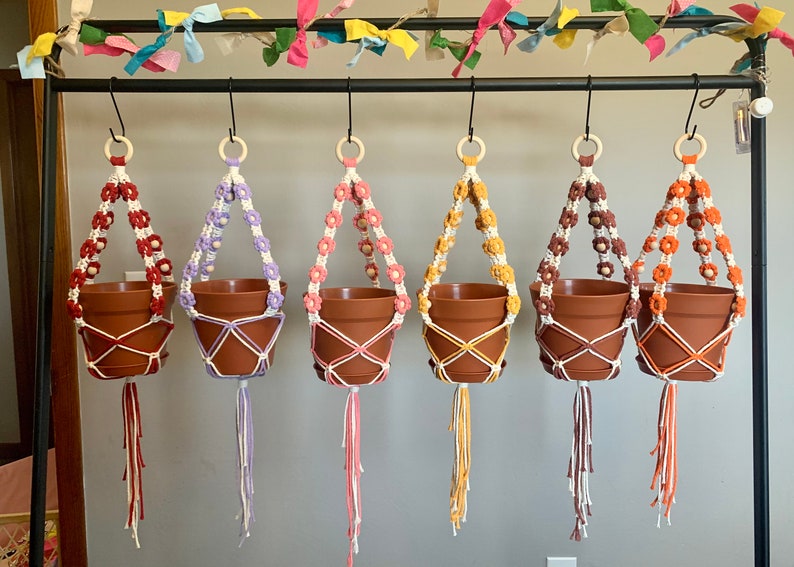 Peut inclure: Cinq suspensions de plantes en macram&eacute; avec des fils de diff&eacute;rentes couleurs et des perles en bois. Chaque suspension est dot&eacute;e d'un pot en terre cuite.