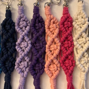 Puede incluir: Un conjunto de diez llaveros de macram&eacute; de colores con anillas de plata. Los llaveros est&aacute;n hechos con una variedad de colores, incluyendo azul, morado, rosa y blanco.