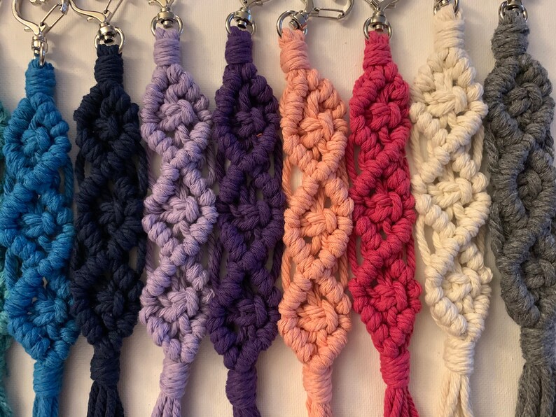 Puede incluir: Un conjunto de diez llaveros de macram&eacute; de colores con anillas de plata. Los llaveros est&aacute;n hechos con una variedad de colores, incluyendo azul, morado, rosa y blanco.