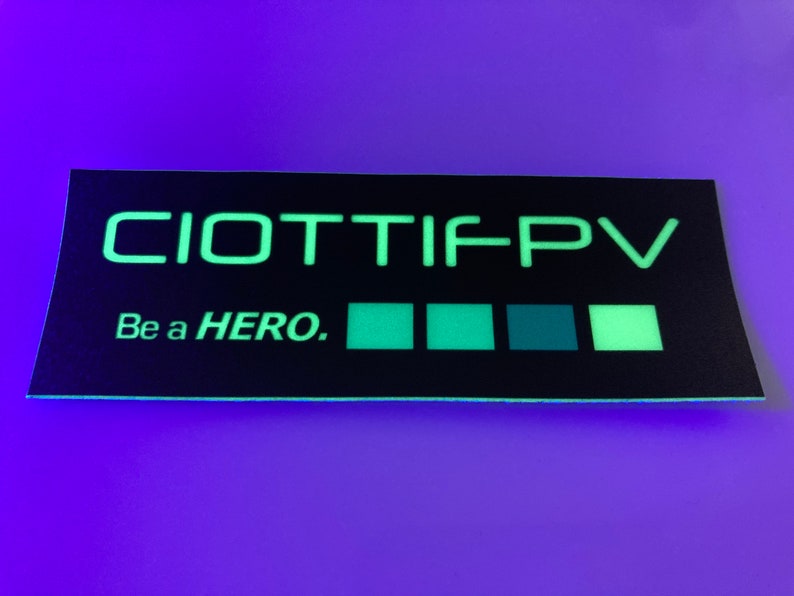 May include: A black and green glow-in-the-dark sticker with the text "CIOTTIFPV" and "Be a HERO." The sticker has five green squares.