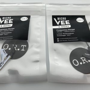 May include: Two white plastic bags with black text and logos. Each bag contains a black and white circular sticker with the text "O.R.T." and a small black and white transmitter with a black cable. The text on the bags reads "MICRO VEE 5.8GHz" and "Frequency Range 5645-5945 Mhz Linear Polarization Coverage: 360° oldradiotransmission Old Radio Transmission".