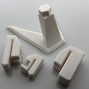 May include: A collection of off-white, geometric jewelry display stands. The set includes a large angled stand, a vertical stand, and three smaller U-shaped stands, all with a textured surface. The stands are designed to showcase jewelry.
