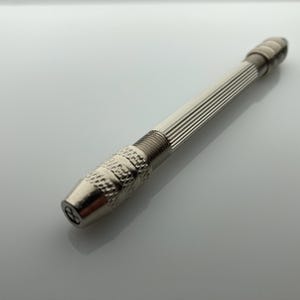 May include: A silver metal hand drill with a ribbed handle and a chuck at the end.