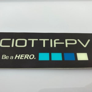 May include: Black and white sticker with the text "CIOTTIFPV" and "Be a HERO."  The sticker has a row of four colored squares: light blue, turquoise, dark blue, and white.