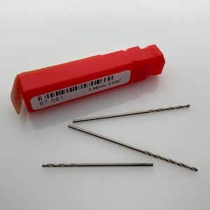 May include: A set of three silver drill bits in a red plastic case. The case has a label that reads "67 561 0.89mm, 0.039"