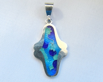 Puede incluir: Un colgante de plata con un diseño de esmalte azul y verde. El colgante tiene forma de lágrima y tiene un bucle en la parte superior para sujetar una cadena.