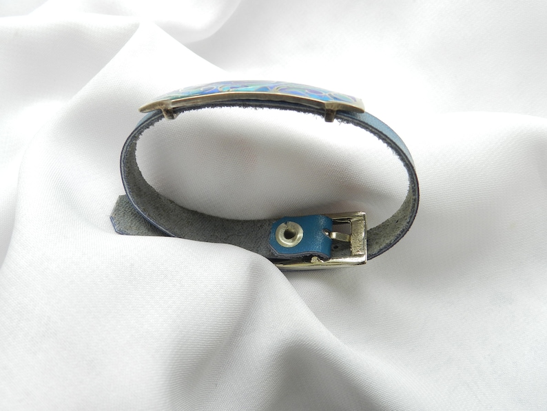 Puede incluir: Un brazalete de cuero azul con una hebilla plateada y una incrustaci&oacute;n de esmalte azul y verde.