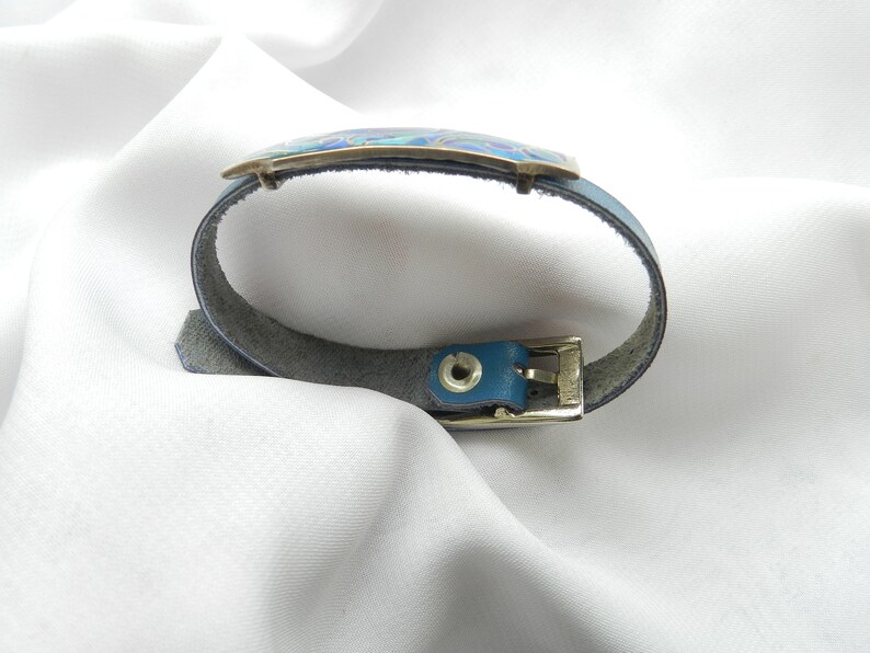 Puede incluir: Un brazalete de cuero azul con una hebilla plateada y una incrustaci&oacute;n de esmalte azul y verde.