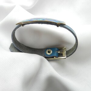 Puede incluir: Un brazalete de cuero azul con una hebilla plateada y una incrustaci&oacute;n de esmalte azul y verde.