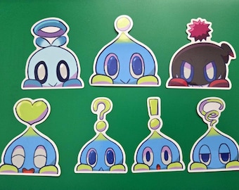 Puede incluir: Conjunto de nueve pegatinas con personajes de dibujos animados azules y amarillos con diferentes expresiones. Los personajes tienen ojos grandes y asoman por detrás de un borde blanco. Las pegatinas son perfectas para añadir un toque de fantasía a los portátiles, las botellas de agua o los diarios.