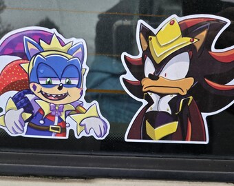 Puede incluir: Dos pegatinas de dibujos animados con personajes de la franquicia Sonic the Hedgehog. Una pegatina representa un erizo azul con un atuendo de bufón y una corona. La otra muestra un erizo negro con un atuendo real.