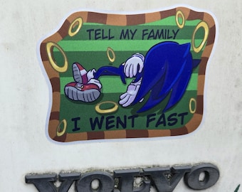 Puede incluir: Una pegatina con Sonic el Erizo tumbado sobre un fondo verde y marrón con anillos dorados. El texto dice "TELL MY FAMILY I WENT FAST". La pegatina está sobre una superficie blanca.