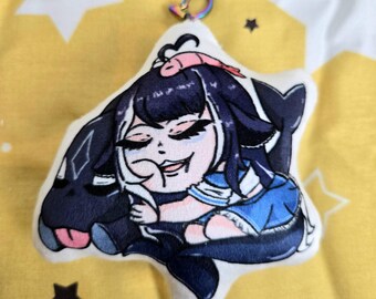 Puede incluir: Llavero de peluche con un personaje de dibujos animados con cabello negro y un atuendo azul, abrazando a una criatura azul oscuro. El llavero tiene un cierre de arcoíris y está sobre un fondo amarillo.