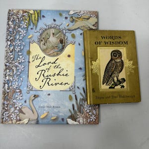 Puede incluir: Dos libros antiguos. Uno tiene una cubierta azul con el título "The Lord of the Rushie River" y una ilustración de cisne. El otro es dorado con una ilustración de búho y el título "Words of Wisdom".