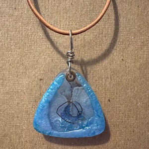 May include: A blue triangular pendant with a silver wire design inside, hanging from a brown leather cord.