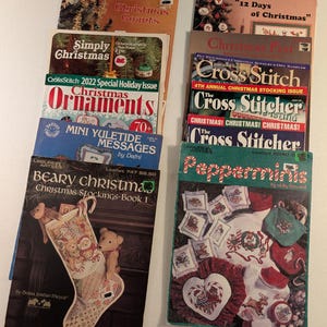 May include: A collection of ten vintage cross-stitch pattern booklets featuring Christmas themes. The covers display various holiday designs including teddy bears, stockings, ornaments, and festive text such as Christmas Counts and Pepperminis.