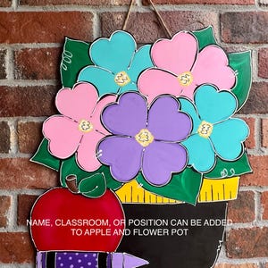 May include: A wooden door hanger with a red apple, a flower pot with pink, purple, blue and green flowers, and a black chalkboard with the text "NAME, CLASSROOM, OR POSITION CAN BE ADDED TO APPLE AND FLOWER POT" and a purple and blue crayon.