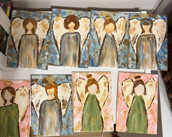 May include: A collection of seven acrylic paintings of angels. Each painting features an angel with white wings, a halo, and a flowing gown. The backgrounds vary, with some featuring blue and gold, and others pink and gold.