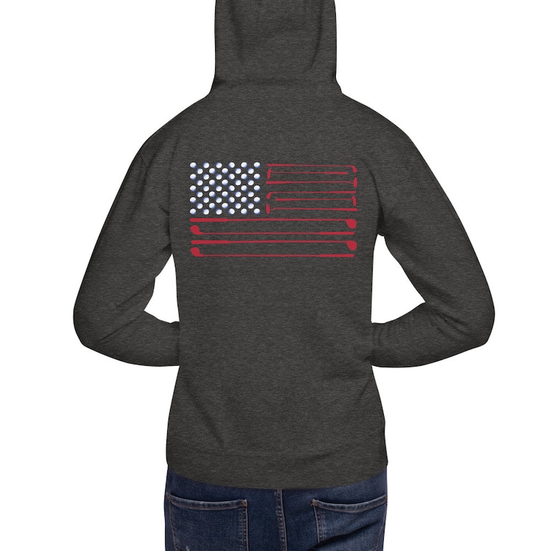 May include: A dark heather grey hoodie with a red, white, and blue American flag design on the back. The flag is made up of golf balls and golf clubs.