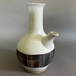 May include: A white ceramic pitcher with a brown and gray geometric pattern. The pitcher has a spout and a tall, slender neck.
