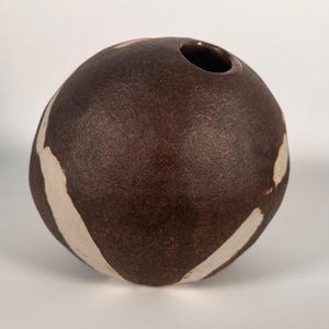 May include: A brown ceramic vase with white abstract designs. The vase is round and has a small opening at the top.