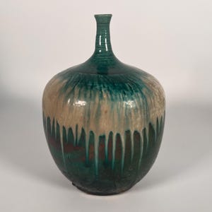 May include: A green and white ceramic vase with a rounded body and a narrow neck. The vase has a drip glaze effect, with white glaze dripping down from the top.