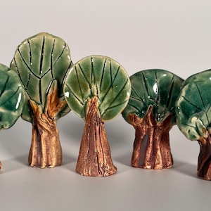 May include: A collection of five ceramic tree figurines. Each tree has a brown trunk and a green, leaf-covered canopy. The trees vary slightly in shape and size, creating a naturalistic display. The glossy finish adds a touch of elegance.