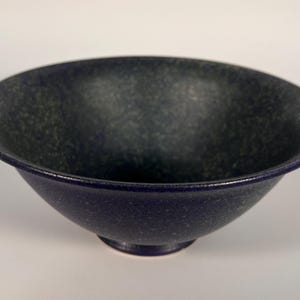 May include: A dark blue ceramic bowl with a speckled green glaze. The bowl has a wide rim and a rounded base.