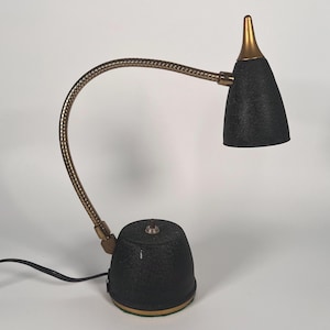 May include: A desk lamp featuring a black textured base and a matching black conical shade with a gold-toned pointed top. The lamp has a flexible, articulated brass-colored neck that allows for adjustable positioning of the light source.