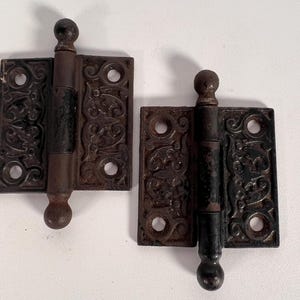May include: Two antique black iron hinges with ornate designs and rounded finials.