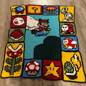May include: A crocheted blanket featuring various characters from the Super Mario Bros. video game series. The blanket is made up of squares with different characters, including Mario, Luigi, Toad, Goombas, and a star. The blanket is a bright and colorful addition to any room.