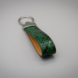 Peut inclure: Un porte-cl&eacute;s en cuir vert et noir &agrave; motif peau de serpent avec un anneau en m&eacute;tal argent&eacute;. L'int&eacute;rieur de la boucle en cuir est de couleur orange clair. Un accessoire &eacute;l&eacute;gant.