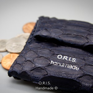Pode incluir: Uma carteira de couro azul escuro com um padrão texturizado e estampado. A carteira está fechada e tem o texto "O.R.I.S. handmade" impresso na parte da frente.
